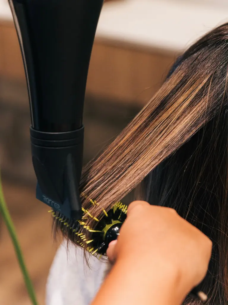 Escova modeladora e secador alisando uma mecha de cabelo castanho iluminado