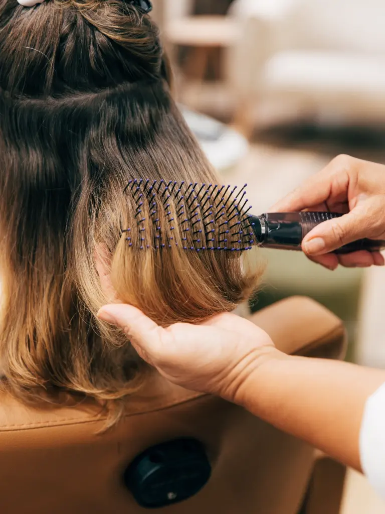 Escova passando por cabelos ondulados com mechas, durante a finalização no salão