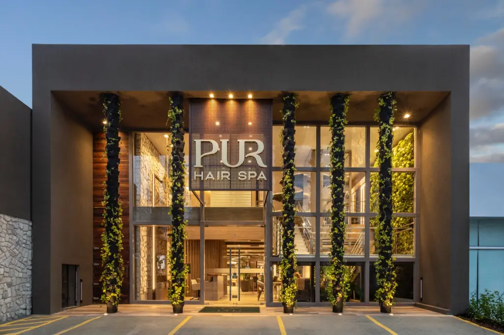 Fachada da PUR Hair Spa ao entardecer, com colunas de plantas e o letreiro iluminado