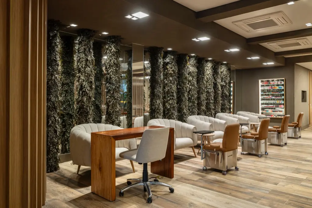Espaço de manicure e pedicure com poltronas claras diante de colunas de folhagens